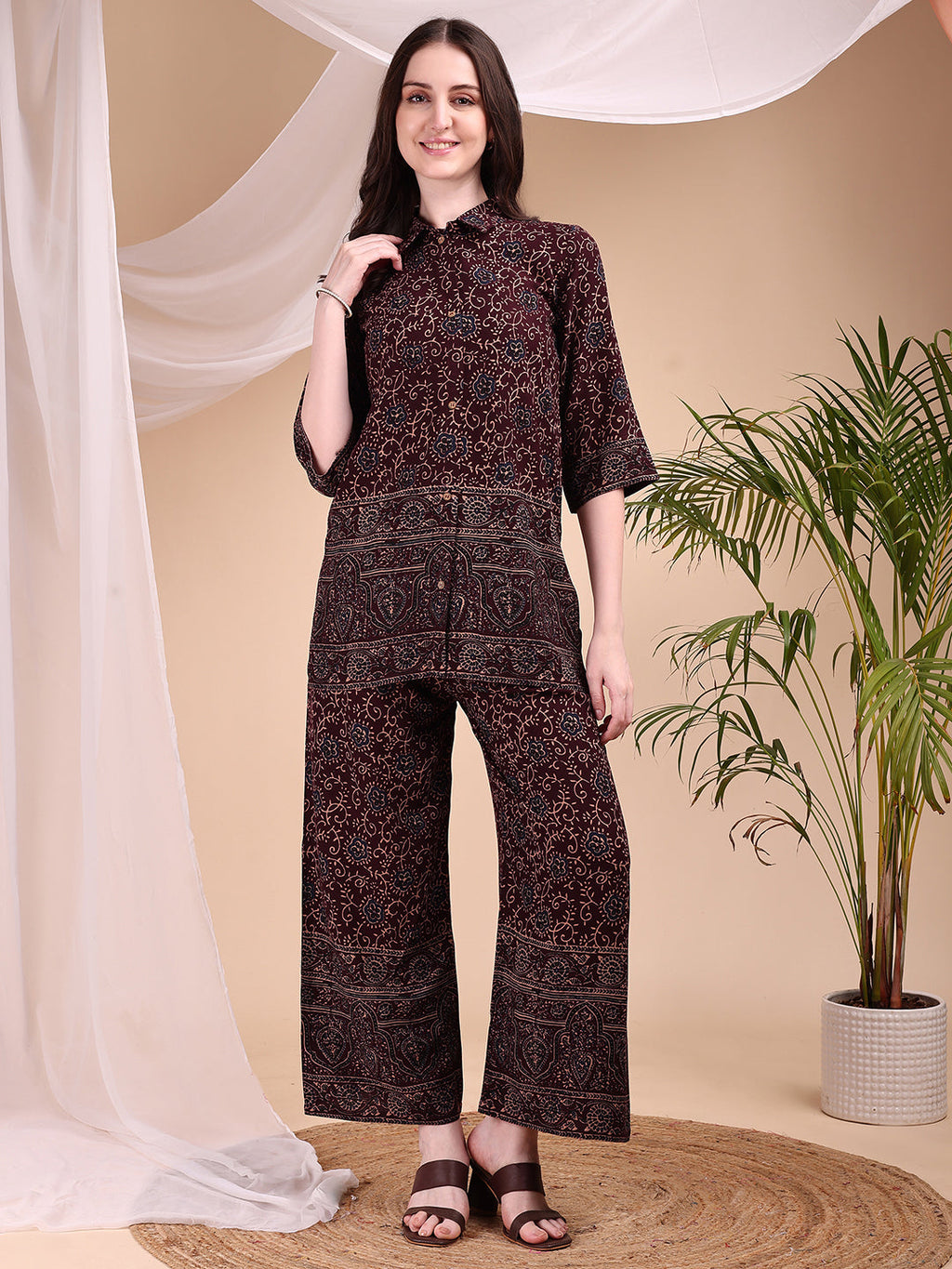 A woman wearing a maroon co-ord set featuring intricate floral and paisley motifs with a collar-neck shirt and palazzo pants.