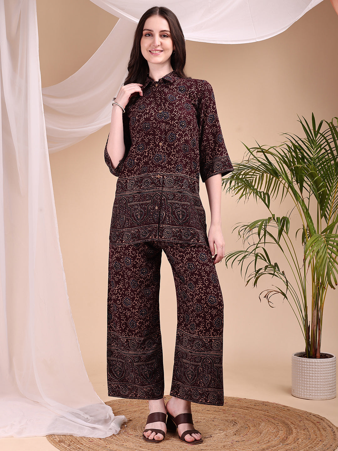 A woman wearing a maroon co-ord set featuring intricate floral and paisley motifs with a collar-neck shirt and palazzo pants.