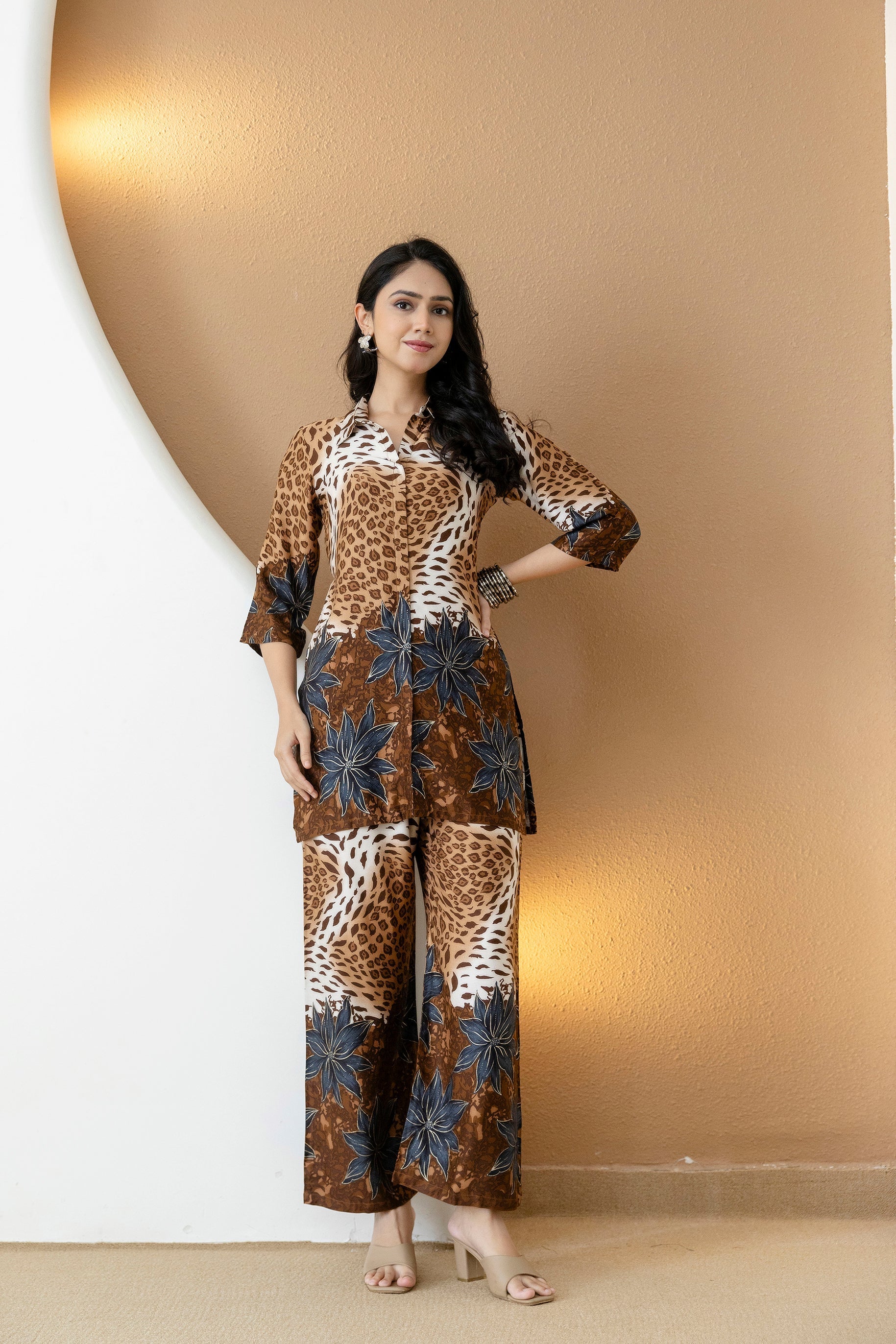 Woman wearing a brown silk co-ord set with animal and floral prints featuring a collar neck and palazzo trousers.