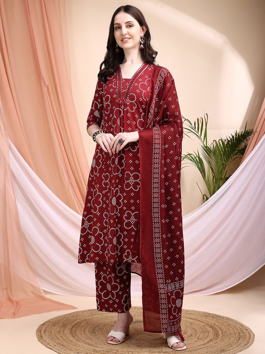 A maroon A-line cotton kurta with Bandhni print, V-neck, 3/4th sleeves, matching pants, and a coordinated dupatta.