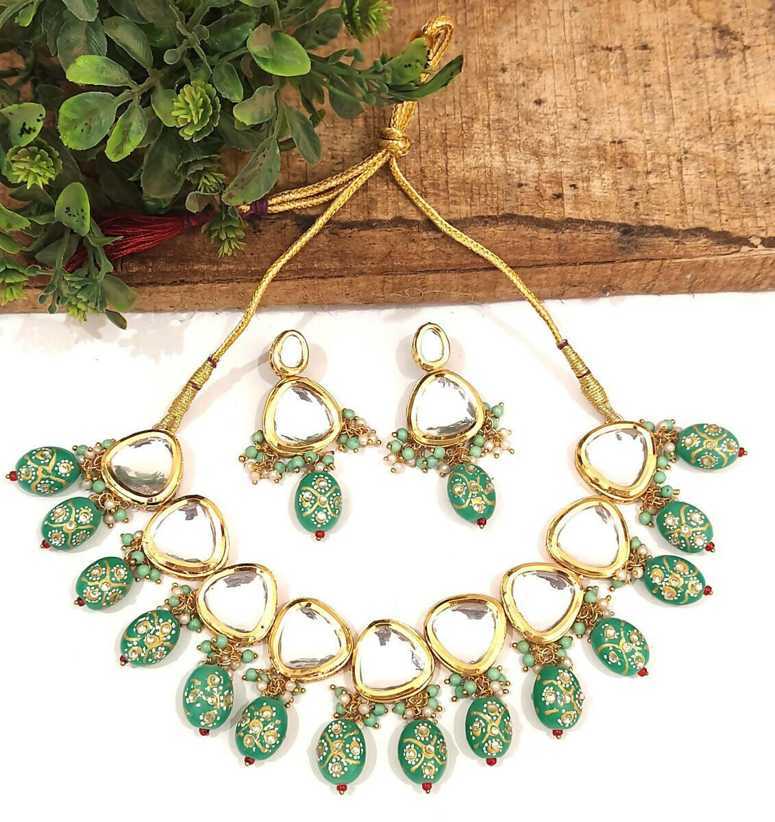 A luxurious green Kundan stone studded jewellery set with gold-plated alloy finish on a neutral background.