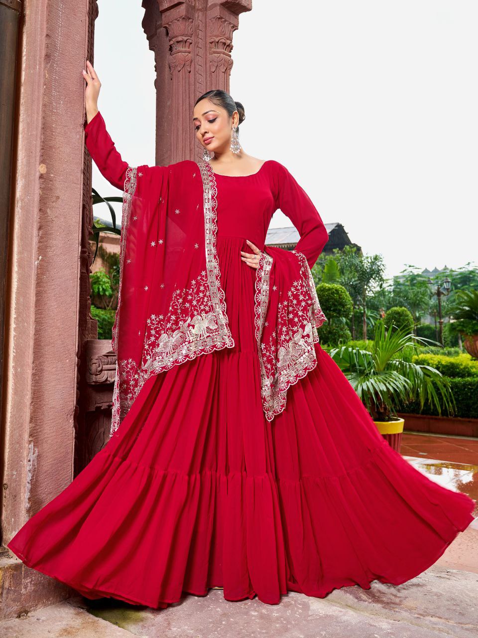 A woman wearing a vibrant red georgette gown with three-layered huge flair and a matching dupatta.