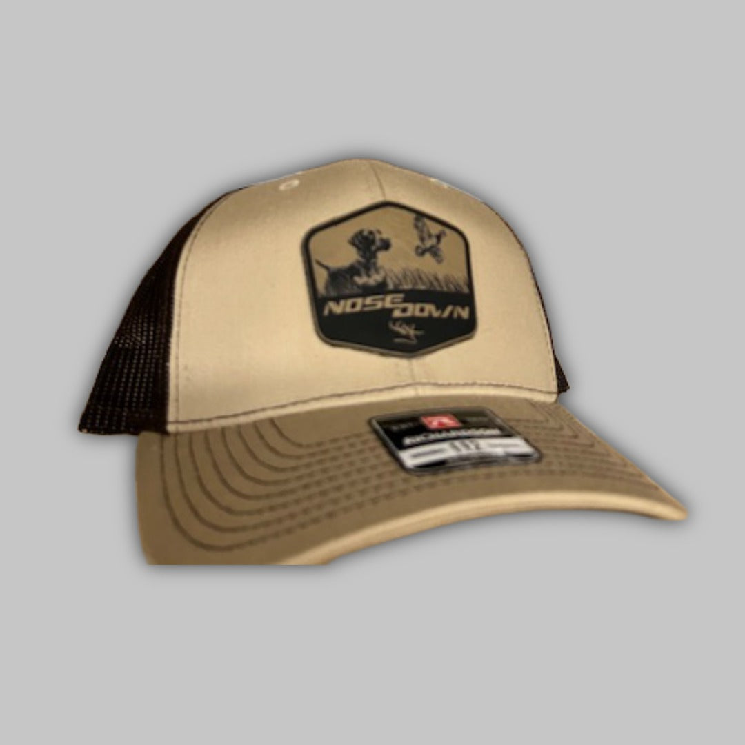 Quail Flush Trucker hat featuring a graphic of a flushing quail and a pointing setter dog.