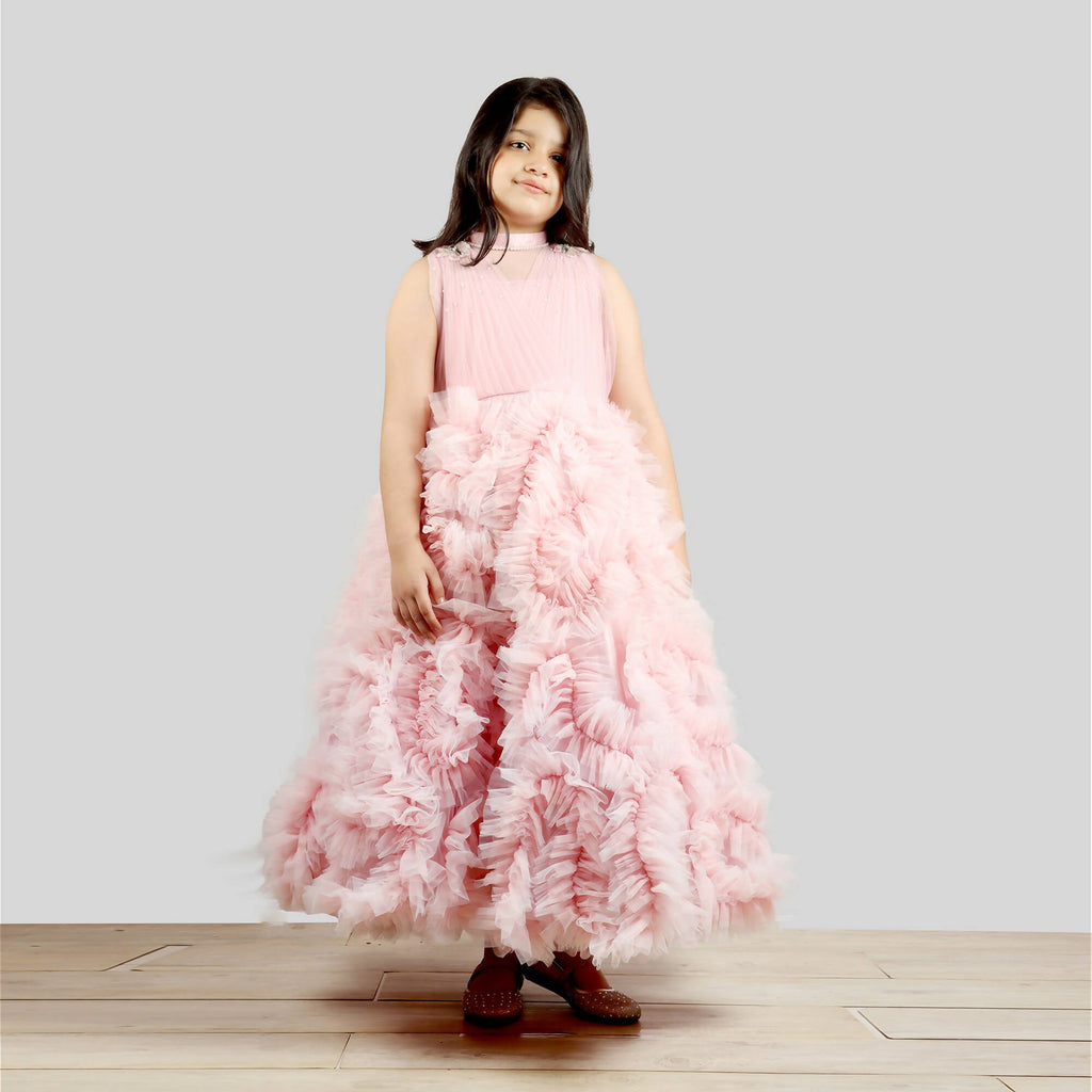 A young girl wearing an old rose gown with a pleated chest and voluminous frilled ghera skirt.