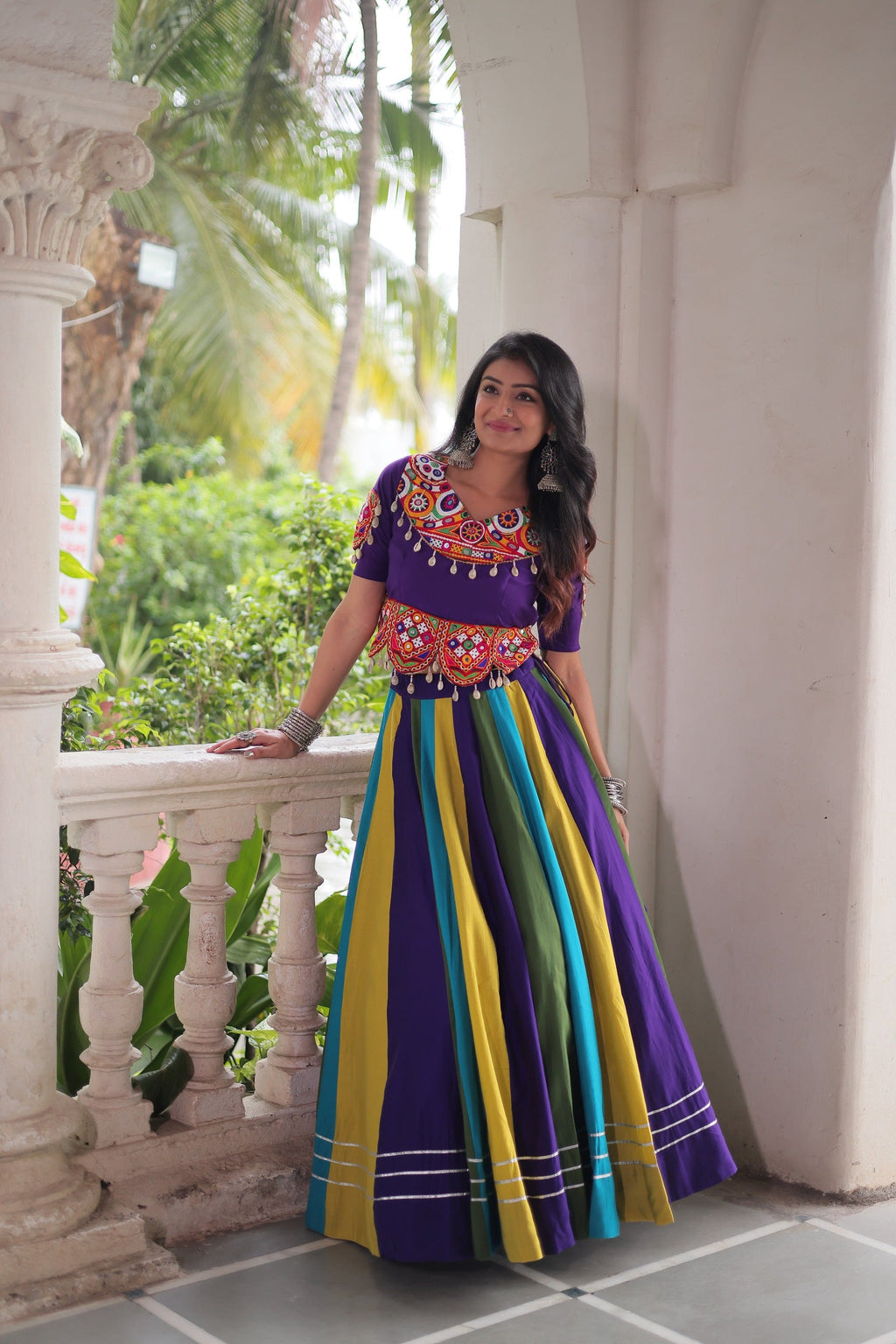 Woman wearing a vibrant violet, yellow, and green striped Gamthi embroidered lehenga with short sleeves for Navratri
