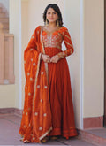 Rust-orange silk gown with intricate gold zari and sequin embroidery, styled with a matching dupatta.