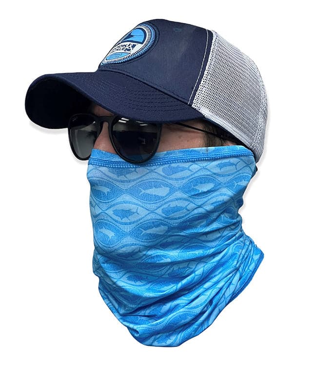 A man wearing a blue neck gaiter with a fish pattern under a navy and white mesh trucker hat.
