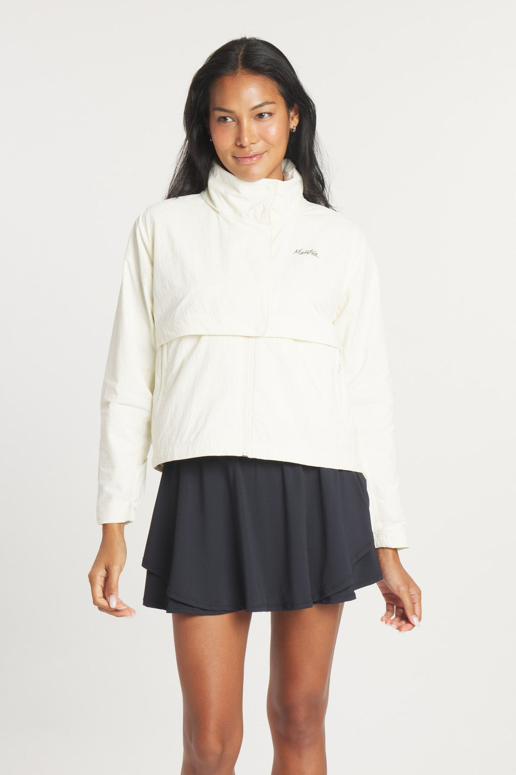 A woman wearing a lightweight birch-colored rain jacket with a high neck and mesh ventilation details.
