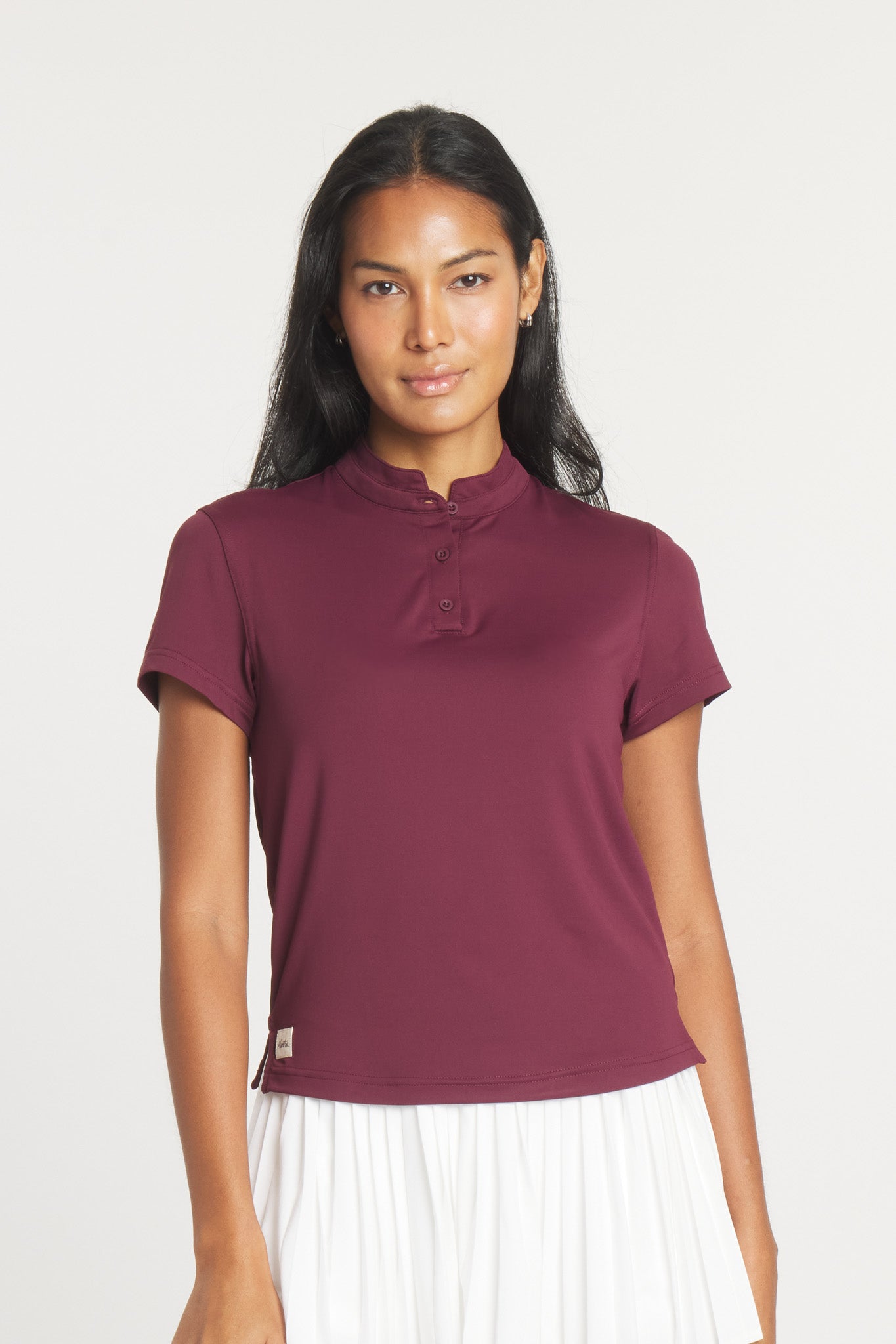 A woman wearing a deep fig-colored short-sleeve polo shirt with a mock collar and a pleated white skirt, shown from front and back views.