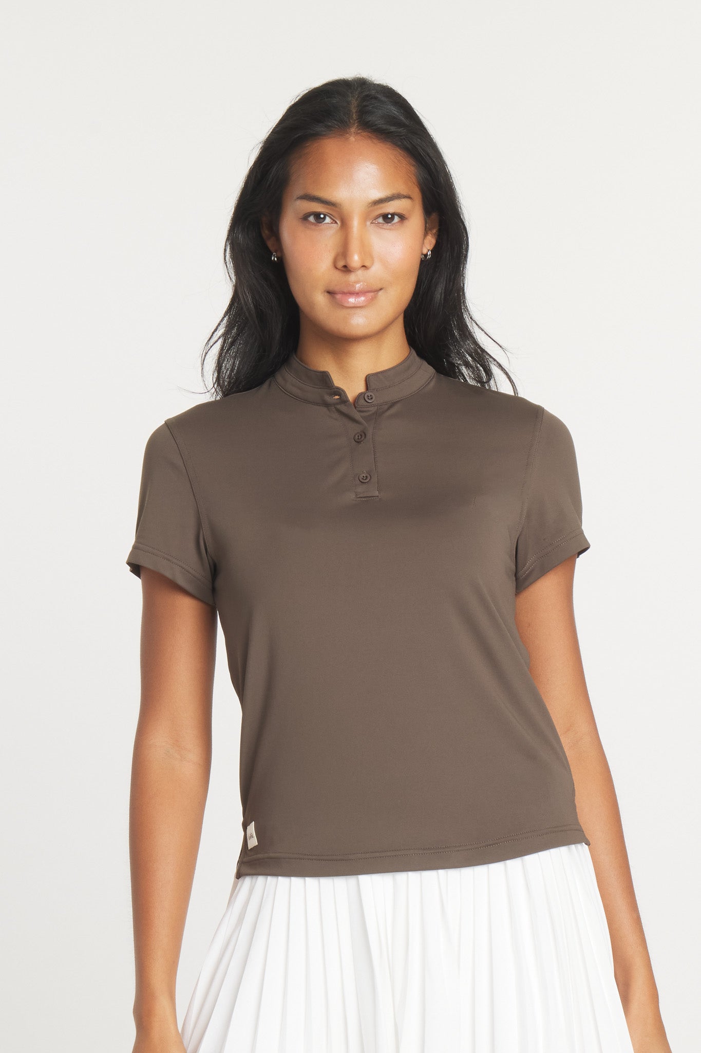 Model wearing a brown Catalyst polo shirt with a mock collar, paired with a white pleated skirt.
