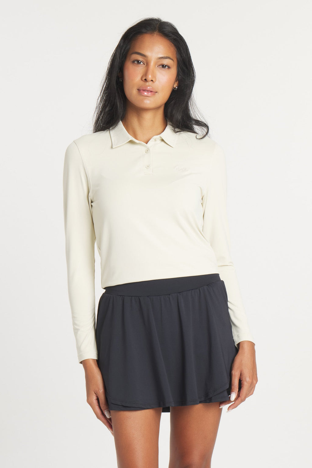 A woman wearing a long-sleeve, Birch-colored Catalyst Polo with a point collar, paired with a black pleated skirt.