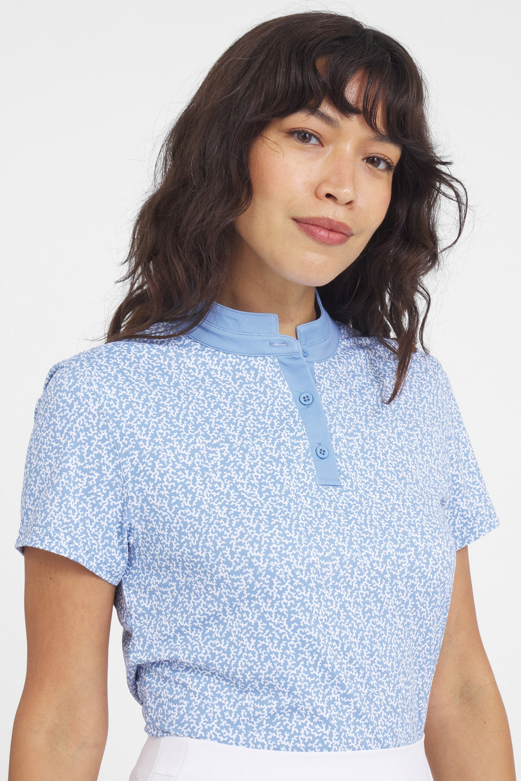 A woman wearing a coral-colored Catalyst polo shirt with a mock collar, featuring a white coral-patterned print.