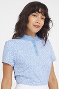 A woman wearing a coral-colored Catalyst polo shirt with a mock collar, featuring a white coral-patterned print.