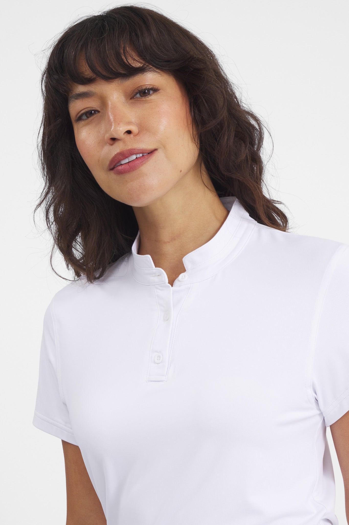 A woman wearing a white Catalyst Polo with a mock collar, styled with a pleated green skirt.