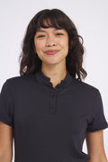 A woman wearing a black short-sleeved Catalyst Polo with a mock collar, paired with a pleated light green skirt.