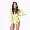 Woman wearing a fitted long sleeve swim cover up in a white and yellow pineapple print with a zip-up collared neckline.