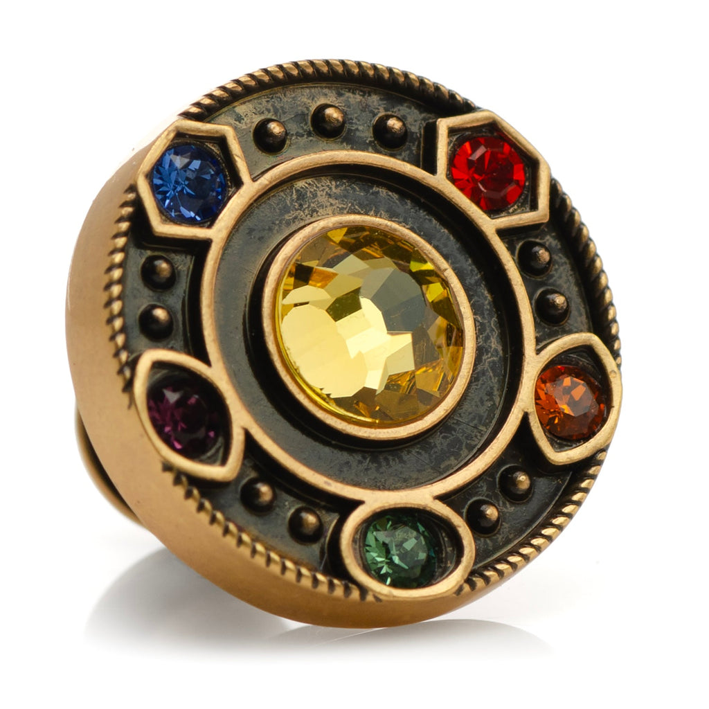 Close-up of a circular antique gold lapel pin featuring six colorful Marvel Infinity Stones against a dark background.