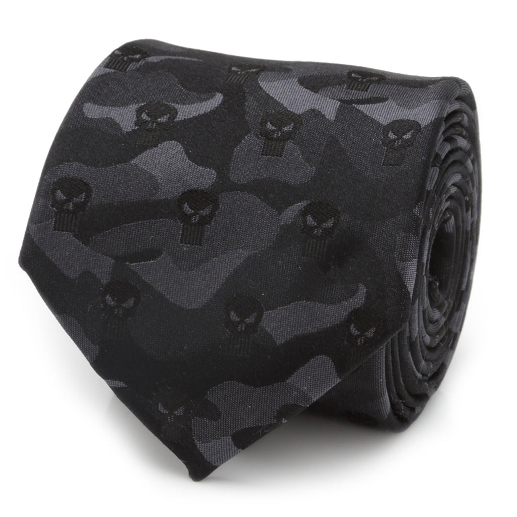 A rolled black silk necktie featuring a subtle camouflage pattern and Punisher skull icons, shown on a white background and styled on a man in a gray suit.