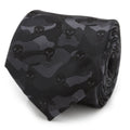 A rolled black silk necktie featuring a subtle camouflage pattern and Punisher skull icons, shown on a white background and styled on a man in a gray suit.