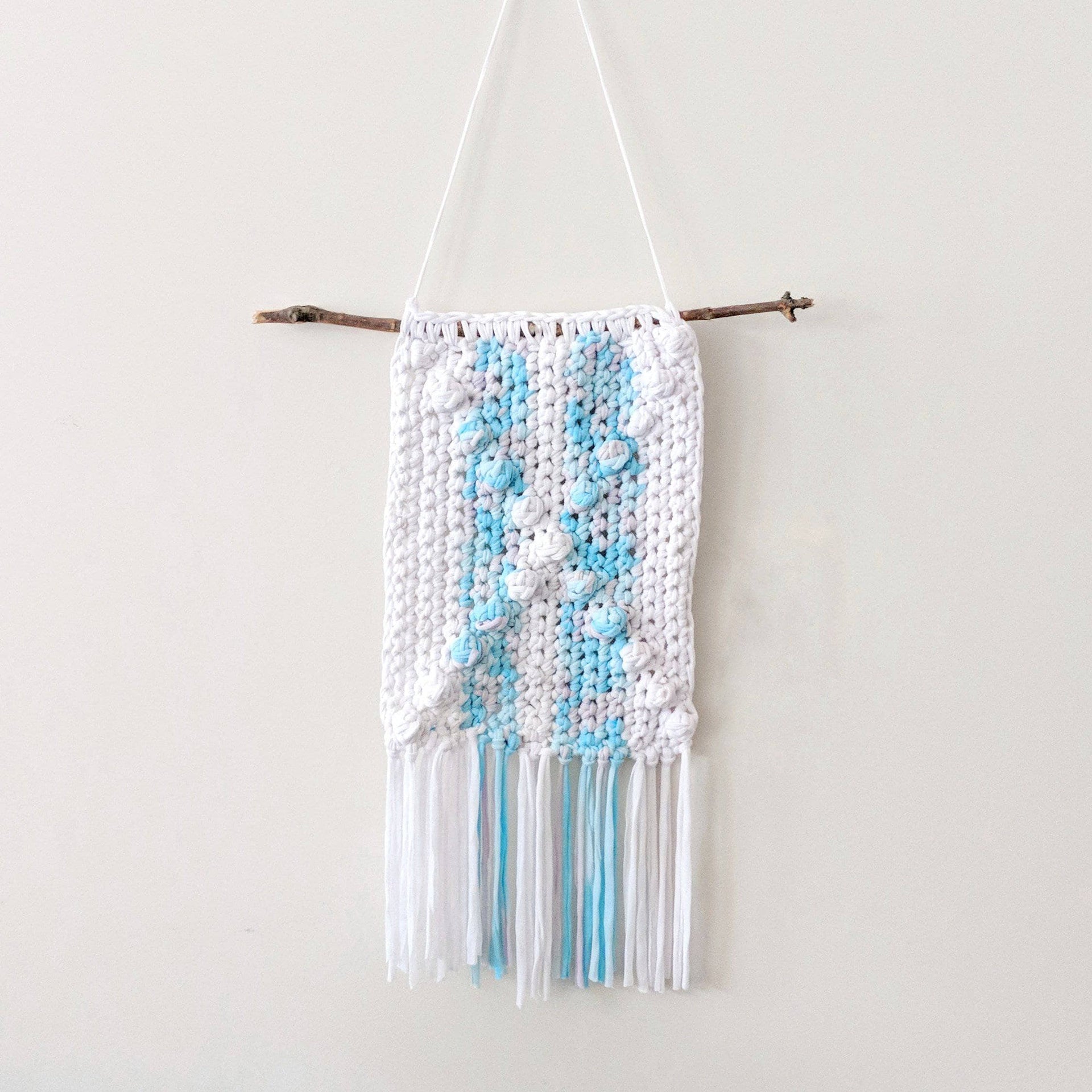 DIY bohemian wall hanging crochet kit featuring white and blue knit fabric, styled for a minimalist bedroom wall.