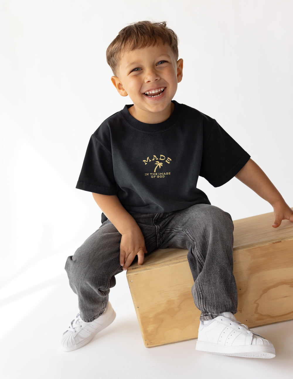 Child wearing a black short-sleeve cotton tee with 'Made in the Image of God' gold graphic print.