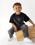 Child wearing a black short-sleeve cotton tee with 'Made in the Image of God' gold graphic print.