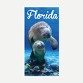 A soft beach towel featuring a photograph of two manatees swimming in blue water with colorful tropical fish and the word Florida written in white script.
