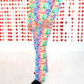 A woman wearing a long-sleeved pajama top and matching pants featuring a colorful rainbow hearts print against a heart-themed backdrop.