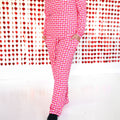 A woman wearing a matching two-piece pajama set with a pink and red checkerboard heart pattern, featuring a button-front top and pants with pockets.