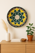 Handcrafted round wicker basket with geometric patterns in forest green, mustard yellow, and maroon on a neutral background.