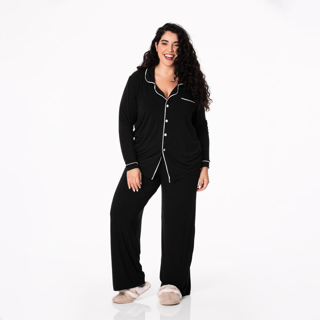 A woman wearing a black long-sleeved collared pajama set with white piping in Midnight and Natural colorway.