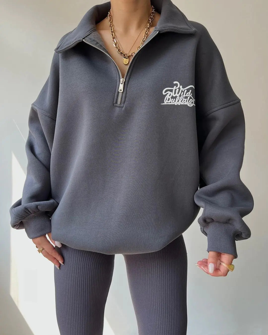 A woman wearing a half-zip pullover fleece sweatshirt with Wild Buffalo embroidery in slab stone gray and caramel colors.