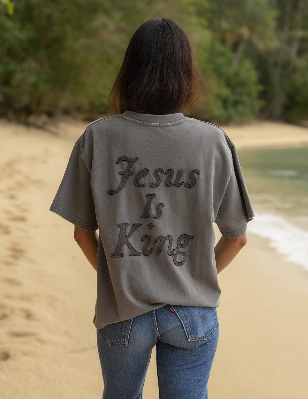 Model wearing a charcoal Jesus Is King heavyweight cotton boxy tee in a minimalist streetwear style