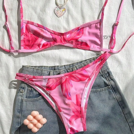 A woman wearing a vibrant fuchsia and pink floral two-piece bikini with a square neckline and tie closure on a beach.