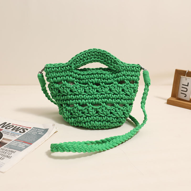 A green and tan woven crochet crossbody bag with a hollow-out design on a neutral background.