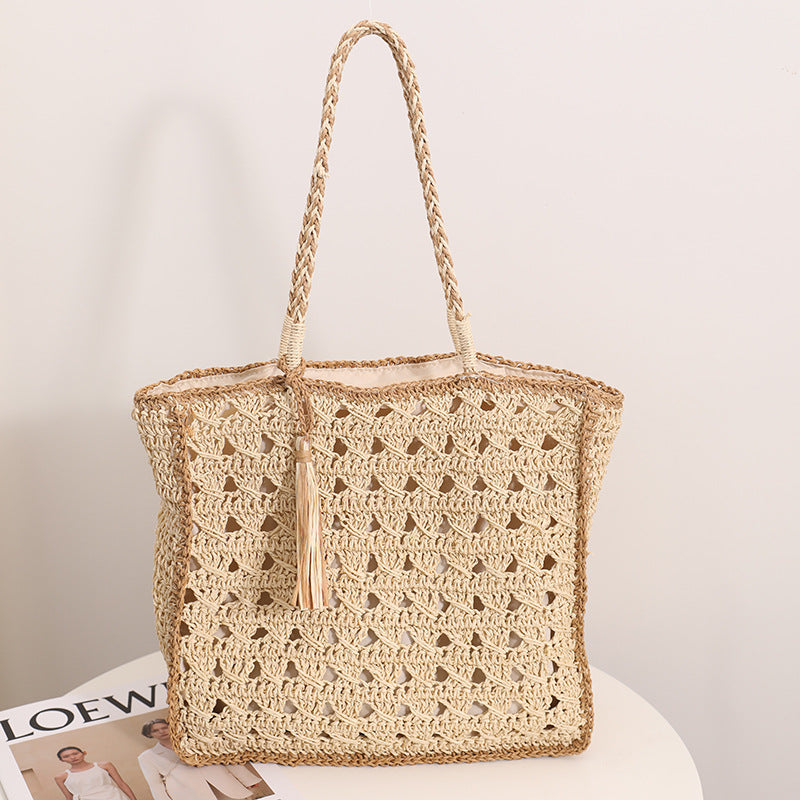 A beige woven straw shoulder bag with a hollow-out pattern and a decorative tassel, shown against a simple background.