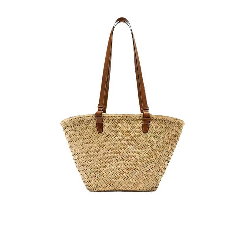 Natural woven straw tote bag with brown leather shoulder straps against a white background