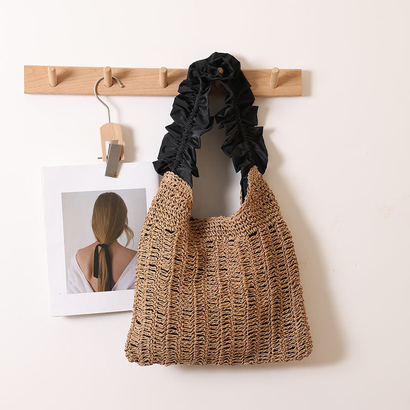 Woven straw shoulder bag with decorative ruffled fabric handle in a natural beige tone.