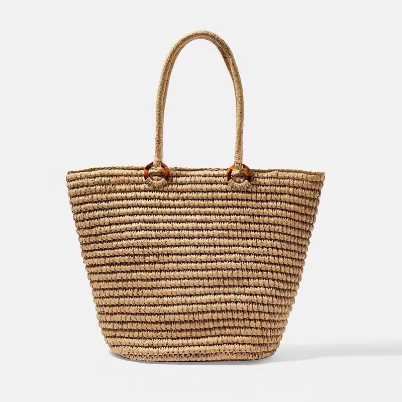 A rustic woven straw tote bag with brown circular handle accents shown against a white background.