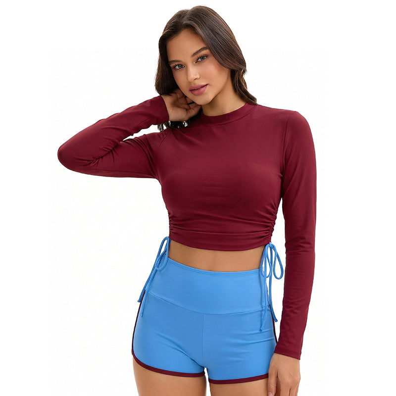A woman wearing a two-piece long sleeve color block swimsuit with ruched and tie details, perfect for a bohemian vacation aesthetic.