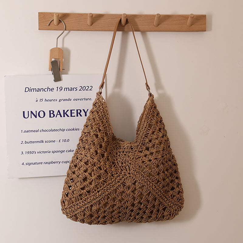 A beige woven hollow out shoulder bag hanging against a wall, suitable for beach vacations and casual summer style.
