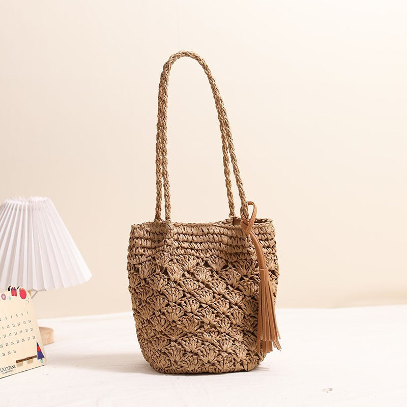 Tan woven straw shoulder bag with decorative tassel and intricate hollow-out pattern
