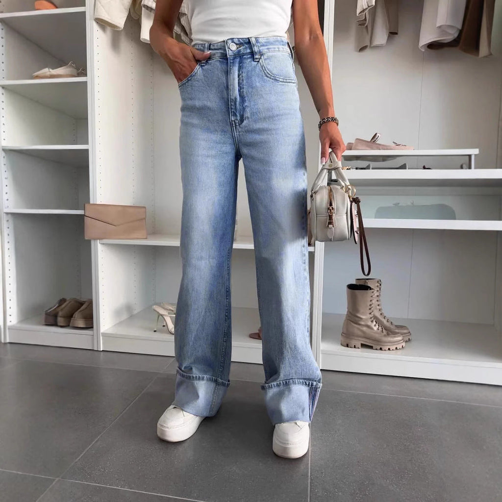A pair of light wash high-rise straight-leg jeans with a distinct cuffed hem worn with white sneakers.