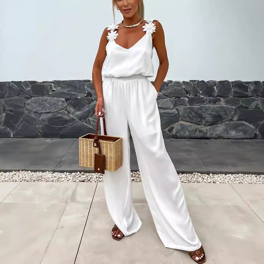 A woman wearing a white sleeveless wide-leg jumpsuit with a V-neck, styled with minimalist accessories.
