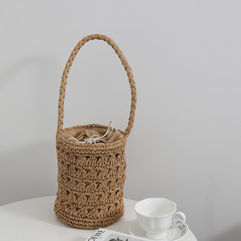 A beige woven rattan bucket bag with a hollow-out design and a protective drawstring interior lining.