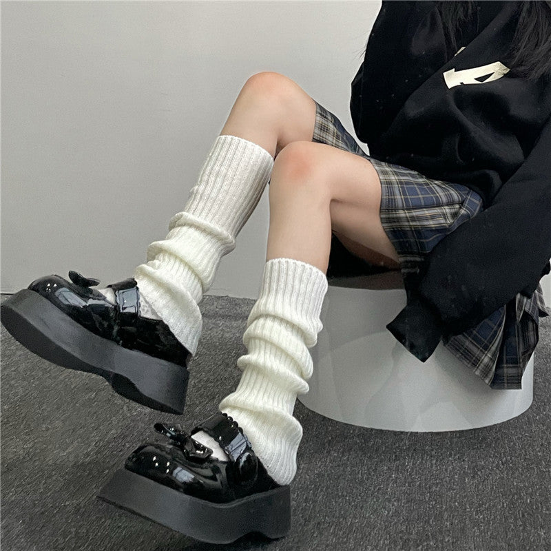 Pair of women's cream knitted long tube calf socks/leg warmers with ribbed texture, styled with platform shoes and a plaid skirt.