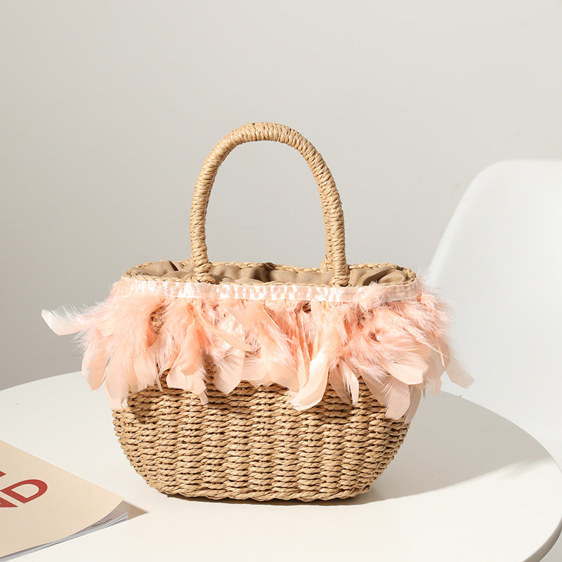 A stylish woven straw handbag featuring a playful pink feather trim and sturdy woven handles, displayed on a table.