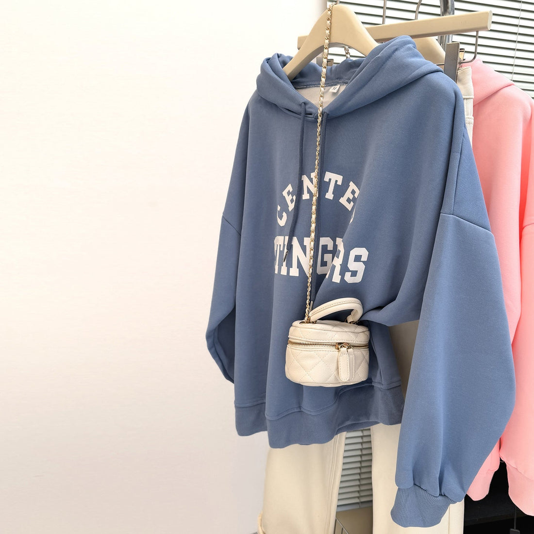 Vintage-inspired women's loose fit hoodie with graphic text print, fleece-lined, shown in blue and cream colors, hanging on a garment rack.