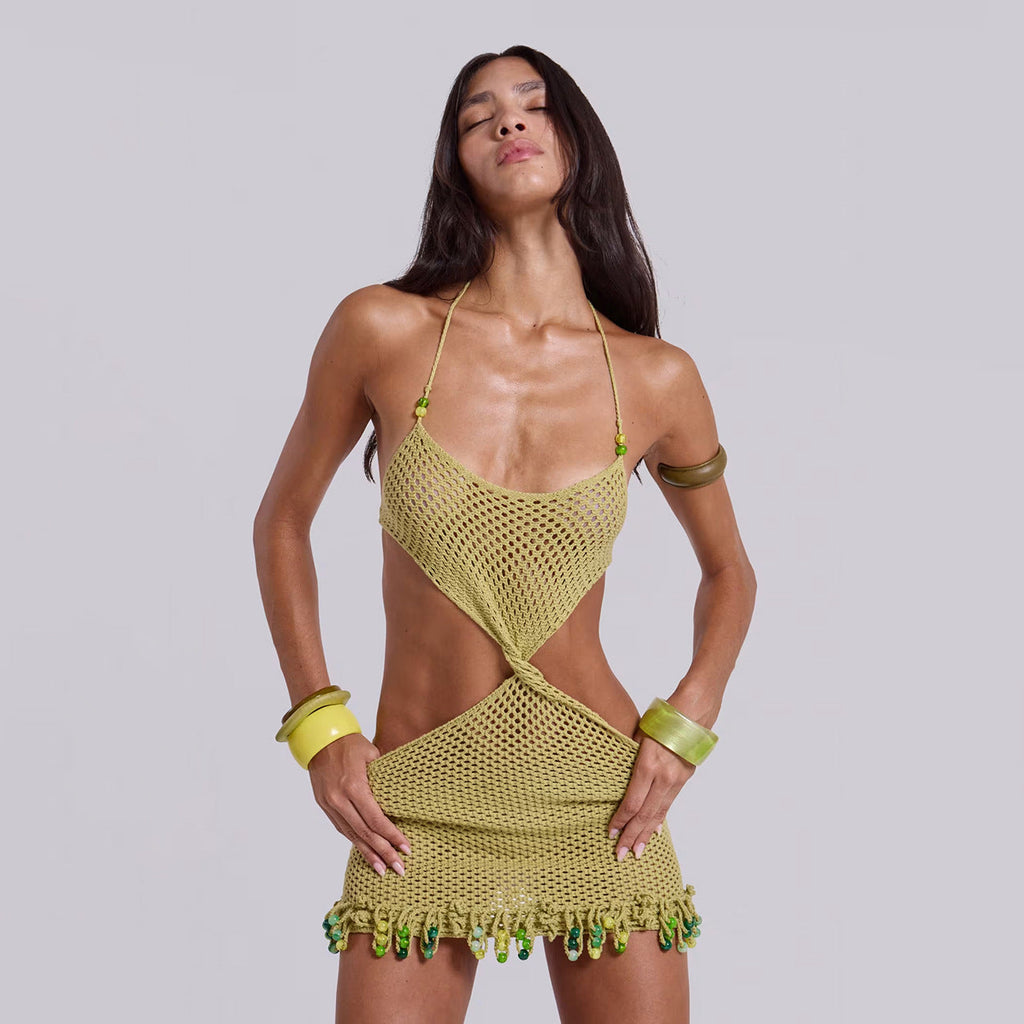 Woman wearing an olive green halter mini dress with cut-out details and tie closure, styled for a boho beach resort look.