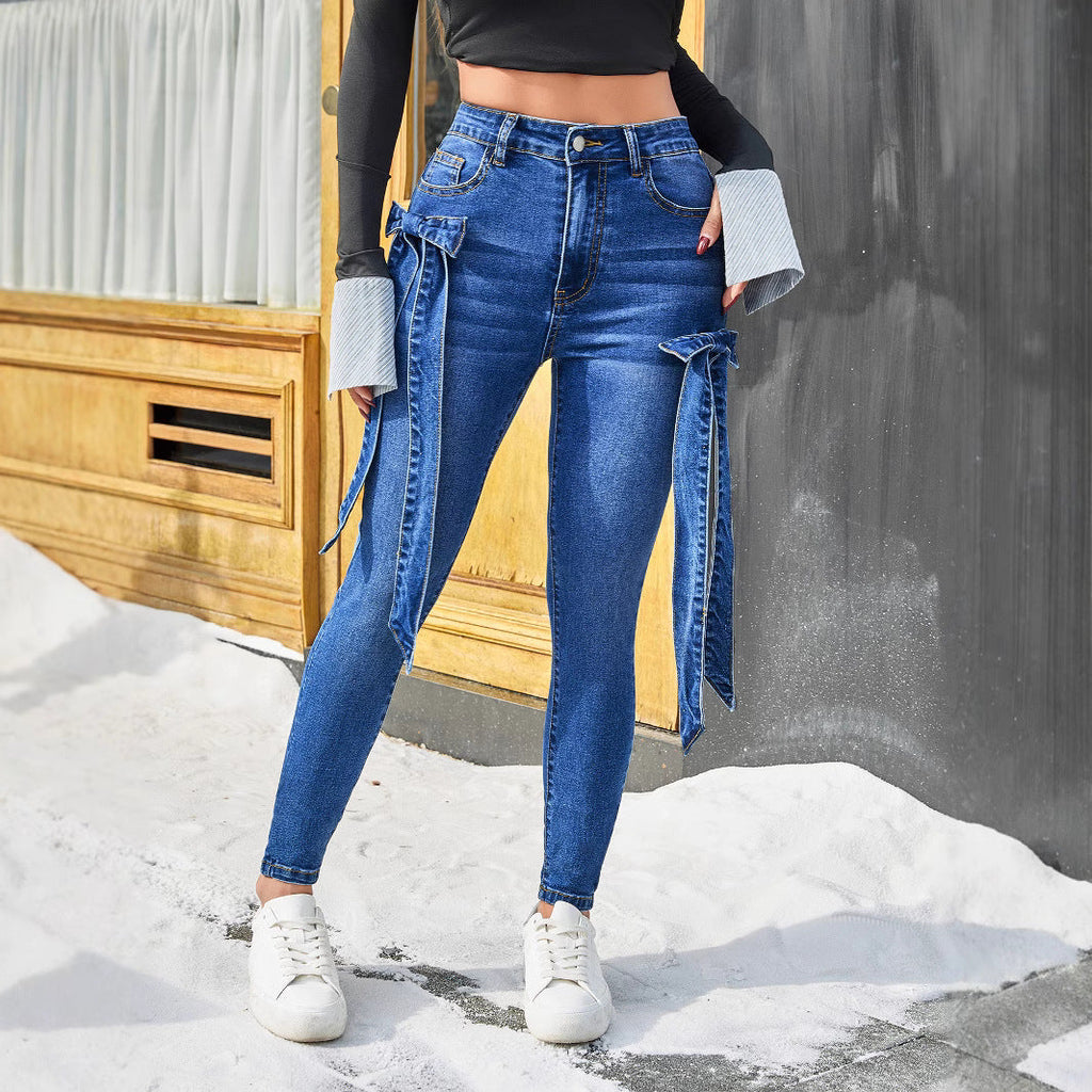 Model wearing dark blue stretch skinny jeans with decorative asymmetric denim bows on the hips.